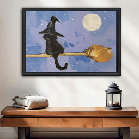 Black cat witch hat riding broomstick framed wall art print, black frame, blue moonlit night oil painting style, displayed above a wooden console table in a warm neutral entryway with lantern decor