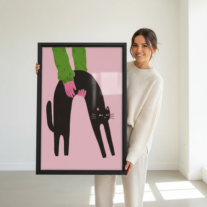 Woman holding large framed black cat arching back being stroked pink background bold illustration art print in black frame showing actual print size in bright white studio