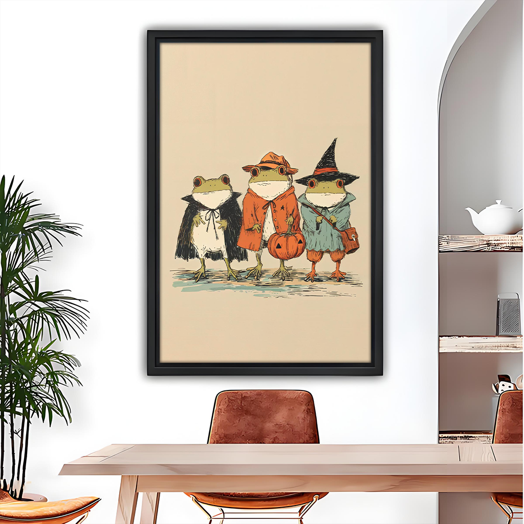 Black-framed Halloween frogs canvas wall art featuring three costumed frogs above a gray sofa with blue pillows.