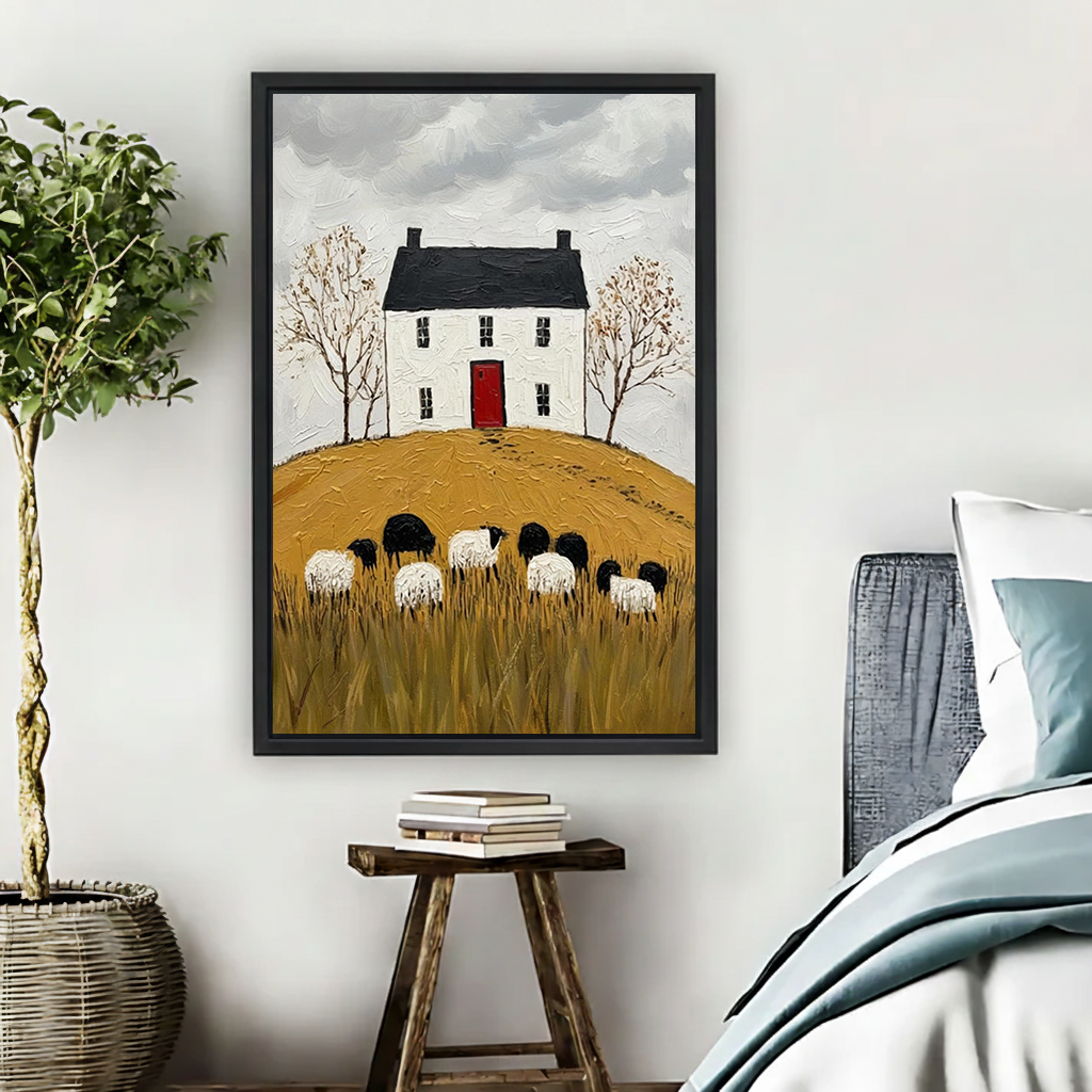 Folk art cottage and sheep canvas wall art in a black frame above a white and gold desk.