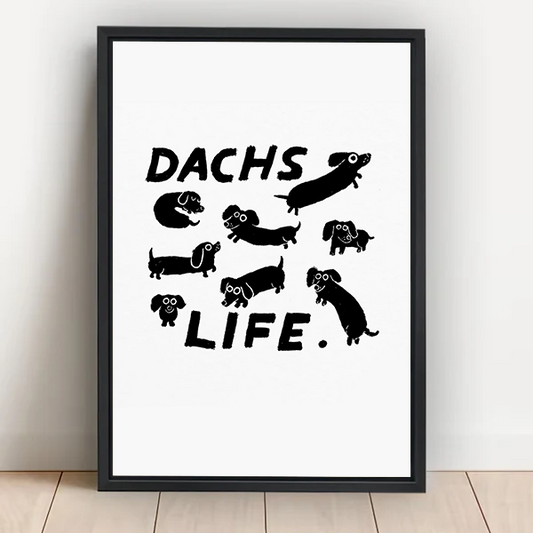 Dachs Life dachshund framed wall art print with black-and-white wiener dog illustrations leaning against white wall