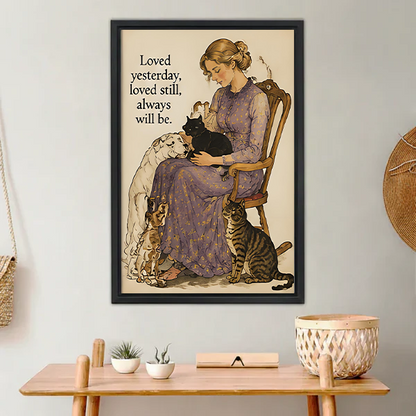 Woman in lavender floral dress sitting on wooden chair holding black cat with white long-haired dog beagle and tabby cat beside her vintage watercolor illustration with loved yesterday loved still always will be quote framed wall art hung on white wall above wooden desk with succulent white bowl and wicker basket in boho home office
