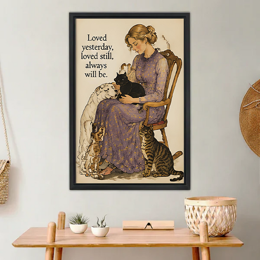 Woman in lavender floral dress sitting on wooden chair holding black cat with white long-haired dog beagle and tabby cat beside her vintage watercolor illustration with loved yesterday loved still always will be quote framed wall art hung on white wall above wooden desk with succulent white bowl and wicker basket in boho home office