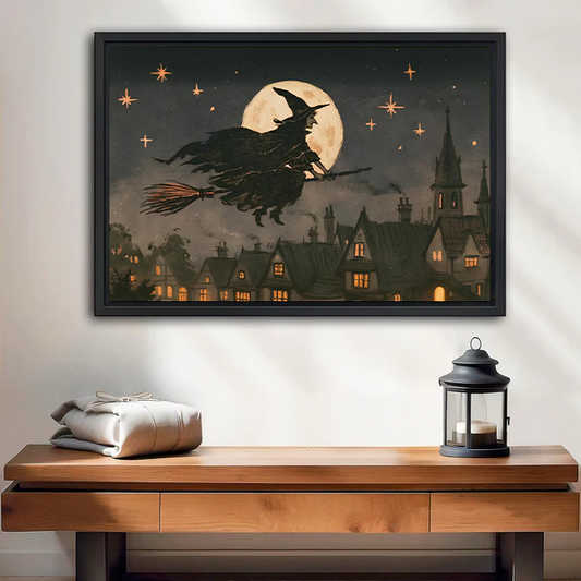 Woman holding black-framed moonlit witch canvas wall art showing a flying witch above a village beneath a golden moon.