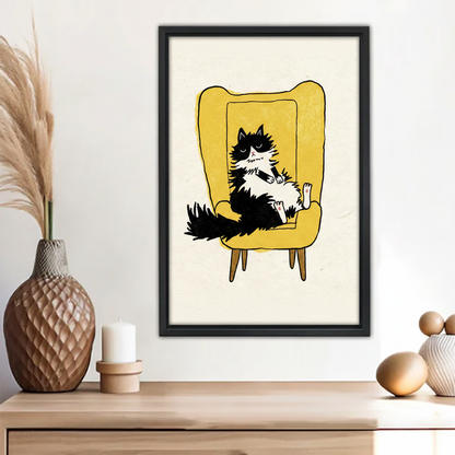 Funny grumpy black and white cat lounging in yellow armchair mid-century wall art print in black frame above wooden sideboard with pineapple vase and white candle in boho living room