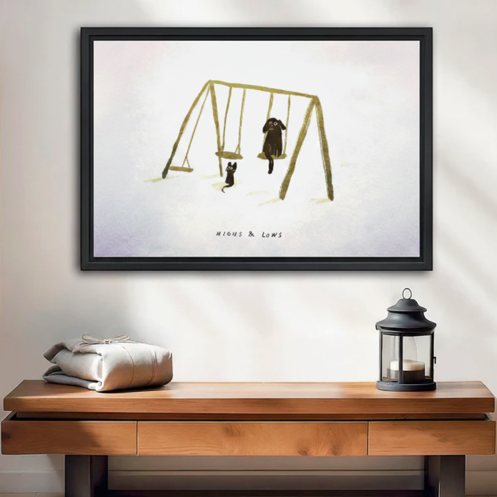 Cat and dog on swing set "Highs & Lows" framed wall art print, black frame, whimsical minimalist illustration, displayed above a wooden console table in a warm neutral entryway