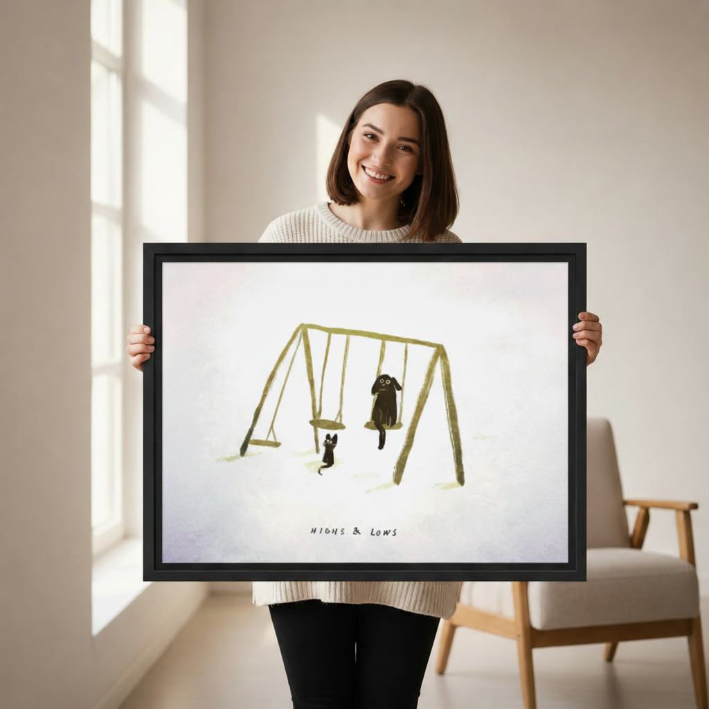 Woman holding large framed cat dog swing "Highs & Lows" wall art print, black frame, whimsical minimalist illustration, showing actual print size in a bright modern room