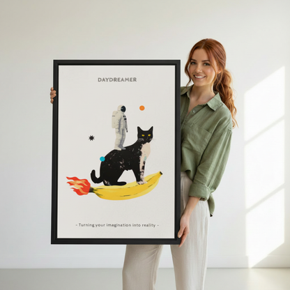 Woman holding large framed daydreamer black cat riding banana rocket astronaut collage wall art print in black frame showing actual print size in bright white studio