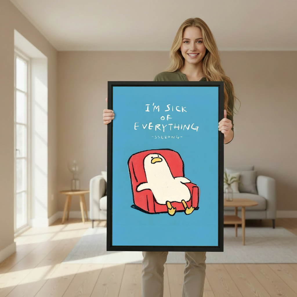 Smiling blonde woman in olive green sweater holding large I'm sick of everything funny duck cartoon framed canvas print with blue background and red armchair in bright beige living room with cream sofa wooden side table and large windows