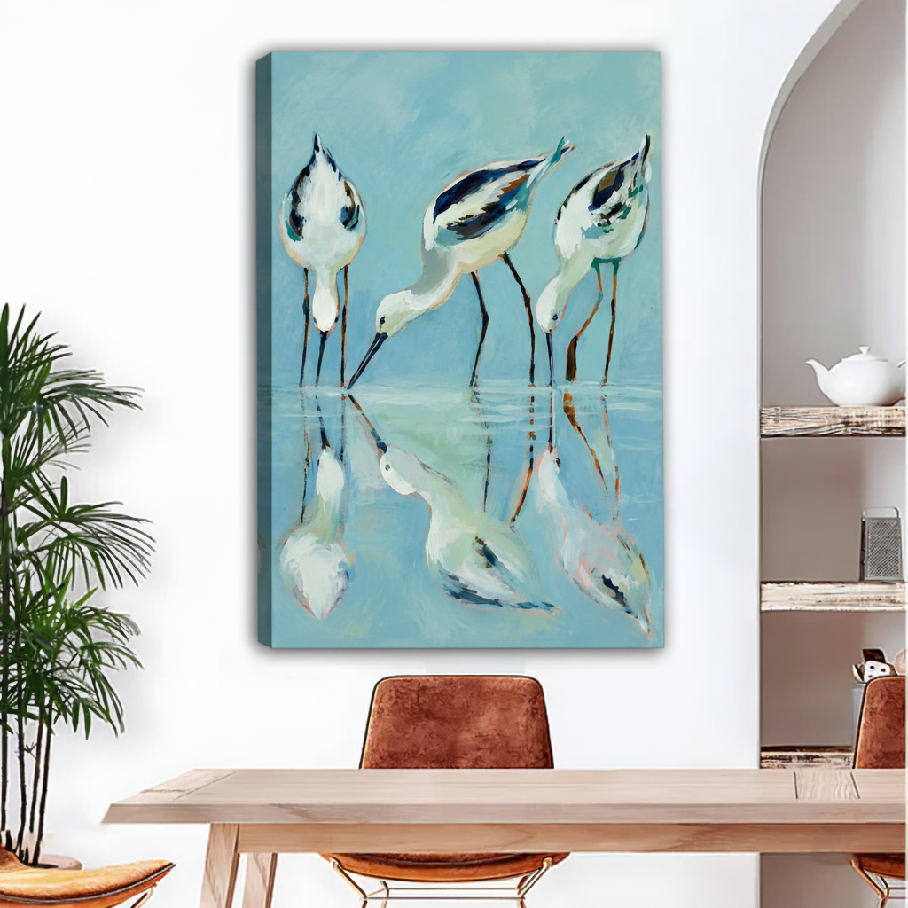 Avocet shorebirds wading water reflection canvas wall art, frameless gallery wrap, teal blue coastal oil painting style, hung above a light wood dining table with leather chairs in a bright modern dining room with indoor palm