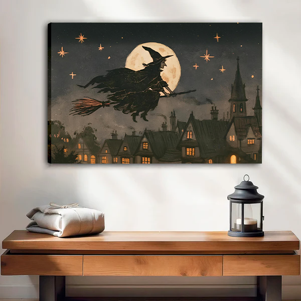 Black-framed vintage moonlit witch canvas wall art above a wooden console table with a lantern and folded blanket.