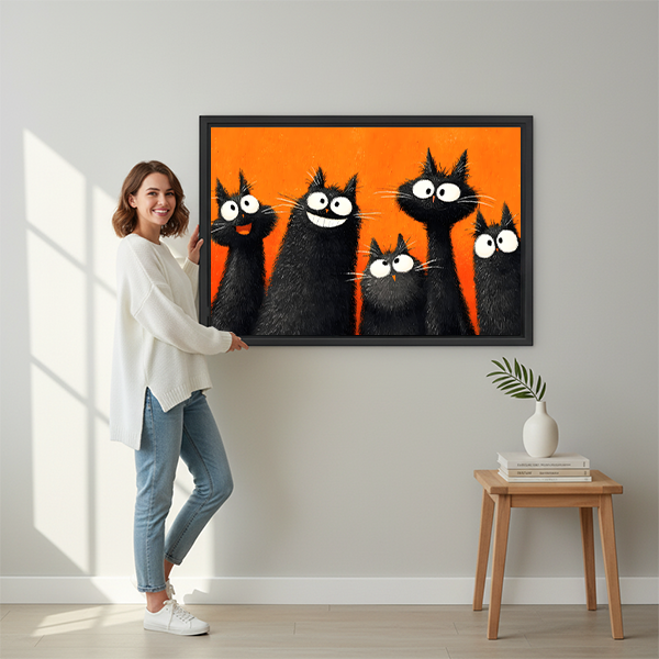 Smiling brunette woman in white shirt and jeans holding large five funny black cats orange background pop art framed canvas print beside wooden stool with white vase and stacked books in bright sunlit hallway