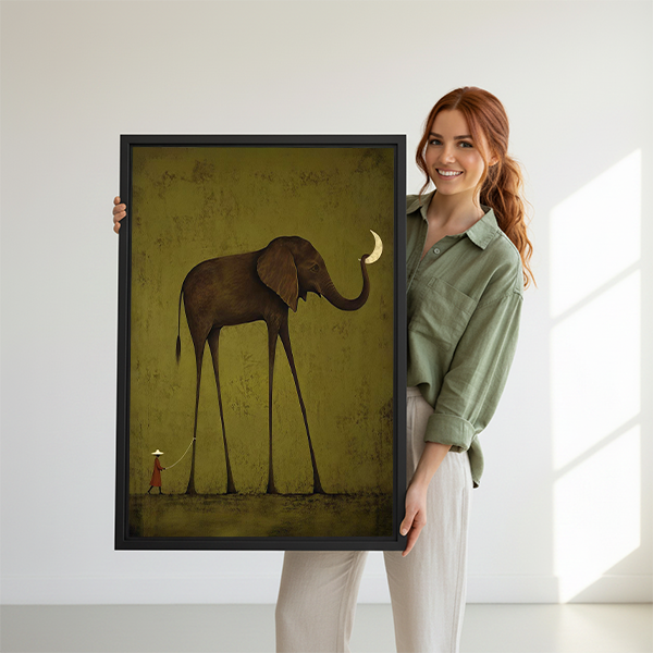 Woman holding framed elephant moon canvas wall art showing a tiny hatted figure beneath an impossibly tall elephant.