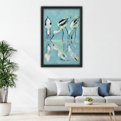Three avocet shorebirds wading water reflection framed art print, black frame, teal blue coastal oil painting style, hung above a light grey linen sofa in a bright Scandinavian living room with indoor palm and round coffee table