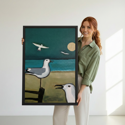Woman holding large framed seagull art print, two coastal birds with teal ocean and golden moon, premium black frame canvas wall art