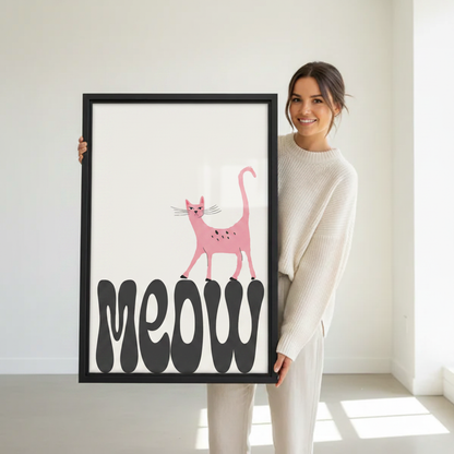 Woman holding large framed pink cat meow typography wall art print in black frame showing actual print size in bright minimalist white studio