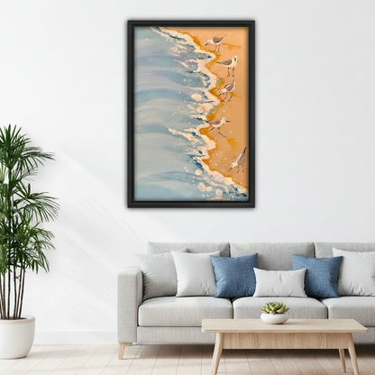 Sandpiper shorebirds on sandy beach with ocean waves framed art print, black frame, warm golden sand coastal oil painting style, hung above a light grey linen sofa in a bright Scandinavian living room with indoor palm and round coffee table