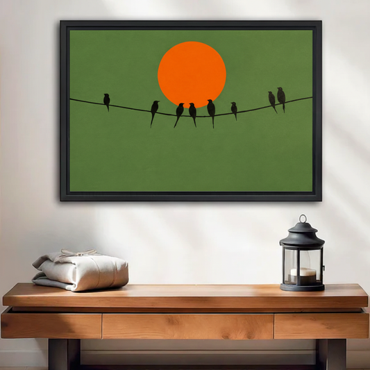Minimalist birds on wire canvas wall art in black floating frame, bird silhouettes against orange sun on olive green background, hung above wooden console table with lantern