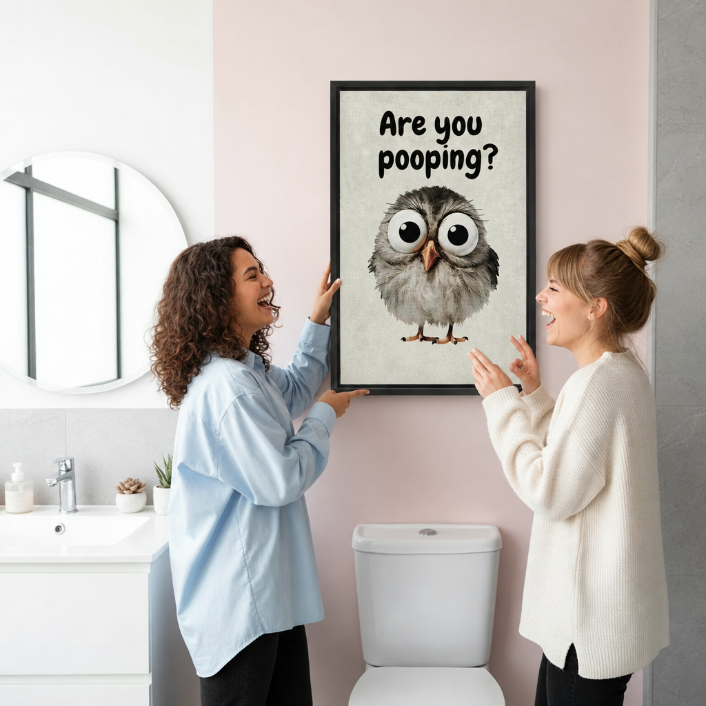 Two women hanging framed are you pooping owl canvas wall art on a bright pink bathroom wall.