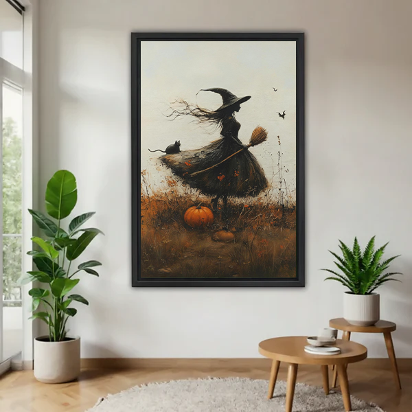 Woman holding black-framed autumn witch canvas wall art depicting a windswept witch, black cat, broom, and orange pumpkin.