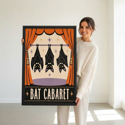 Woman holding black-framed Bat Cabaret canvas wall art featuring three hanging bats, orange curtains and decorative stars.