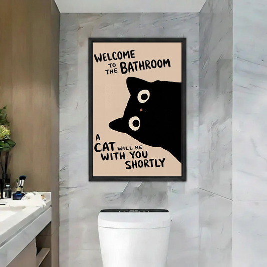 Black-framed black cat bathroom canvas wall art with a funny welcome quote above a toilet against marble walls.