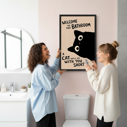 Two women smiling beside framed black cat bathroom canvas wall art with a humorous welcome message.