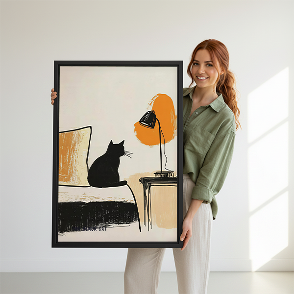 Black framed black cat and lamp canvas wall art with an orange accent, displayed beside plants and tables.