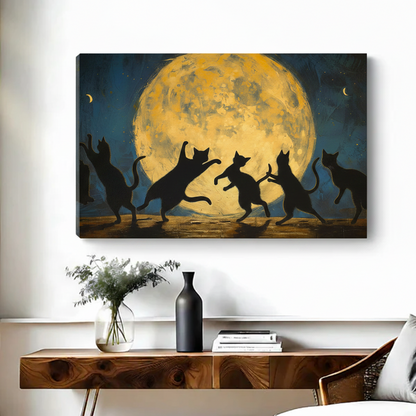Frameless gallery-wrap canvas of five black cat silhouettes dancing and leaping joyfully under a large glowing golden full moon against a deep teal starry night sky, displayed above a walnut console table with a black vase and white floral arrangement