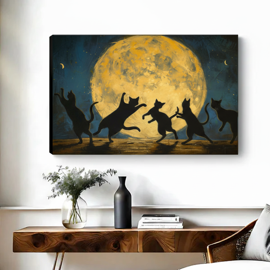 Frameless gallery-wrap canvas of five black cat silhouettes in dynamic dancing poses backlit by a dramatic golden full moon with crescent moons in a deep teal night sky, hung above a walnut console table with a black vase and stacked books