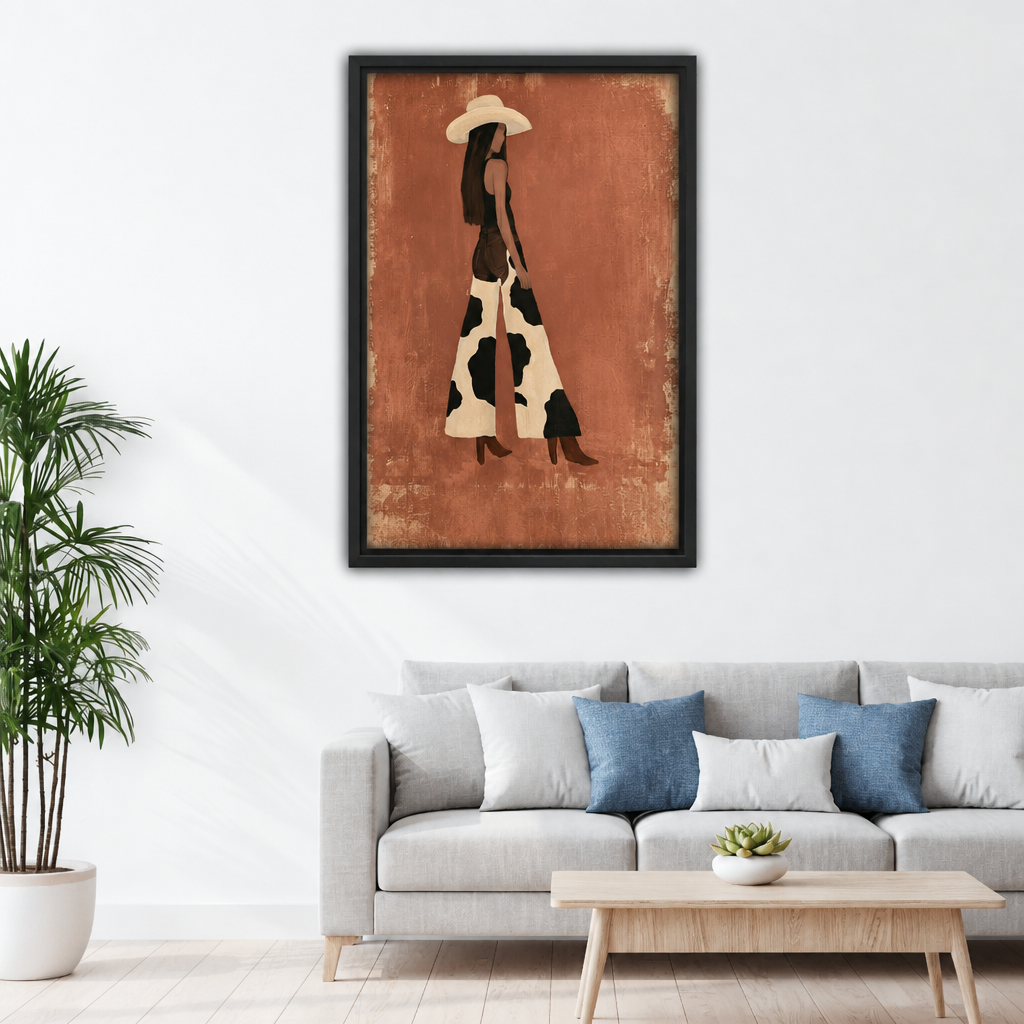 Framed canvas of minimalist boho cowgirl silhouette in wide-brim hat and cow print maxi dress with brown boots on terracotta textured background above grey sofa with blue pillows and wood coffee table