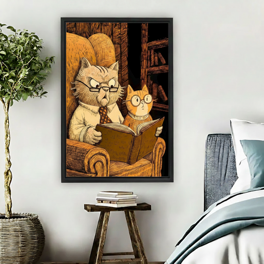 Large black framed wall art of two cartoon cats reading together in a warm library armchair, hung above a wooden stool beside a bed in a minimalist bedroom