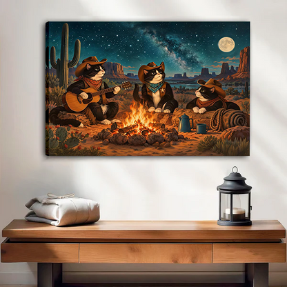 Whimsical cowboy cats campfire canvas wall art in a black frame above a wooden console beside a lantern.