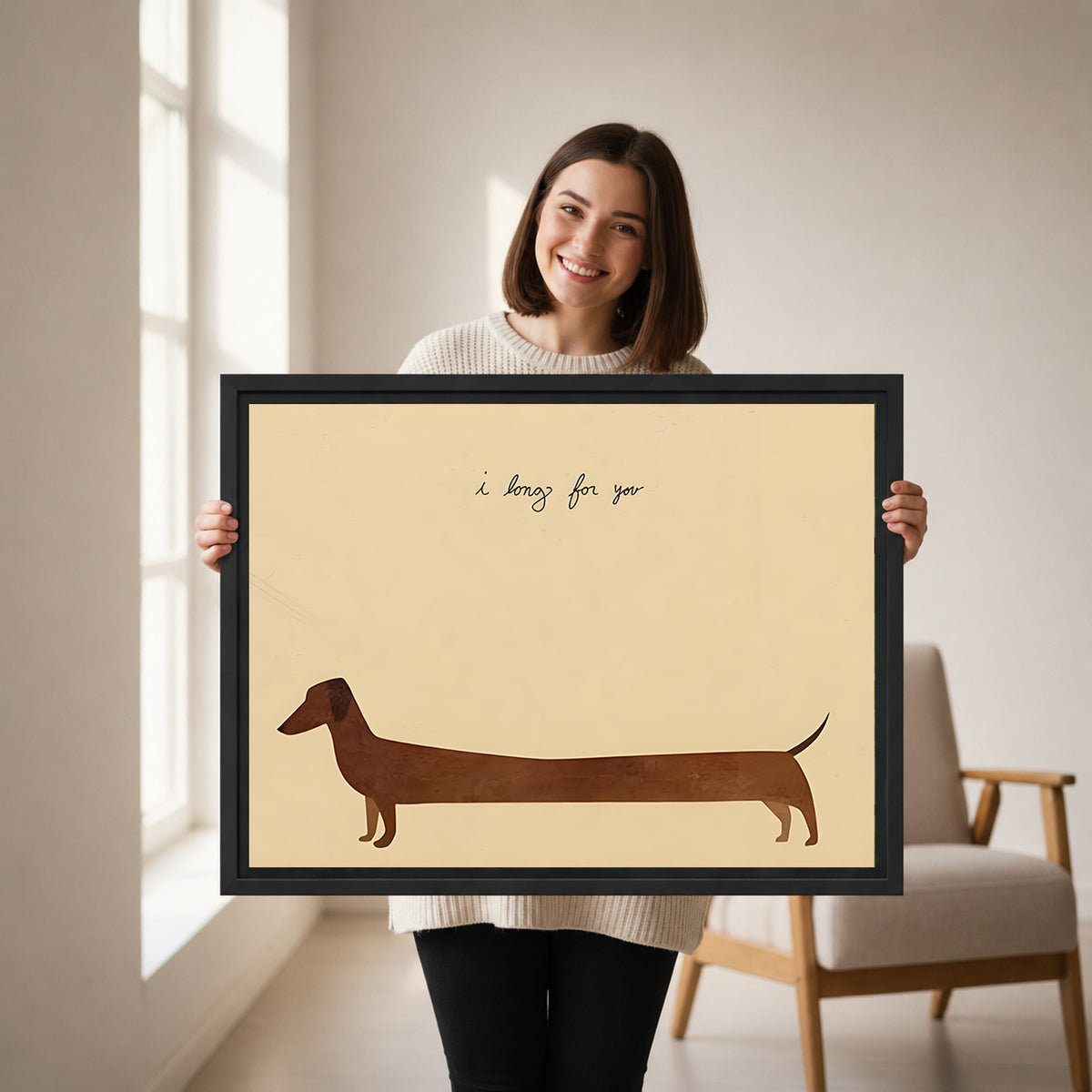 Smiling brunette woman holding large dachshund I long for you minimalist cream background brown silhouette handwritten script black framed canvas wall art size reference in bright white room with wood armchair