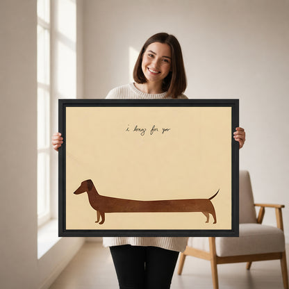 Smiling brunette woman holding large dachshund I long for you minimalist cream background brown silhouette handwritten script black framed canvas wall art size reference in bright white room with wood armchair
