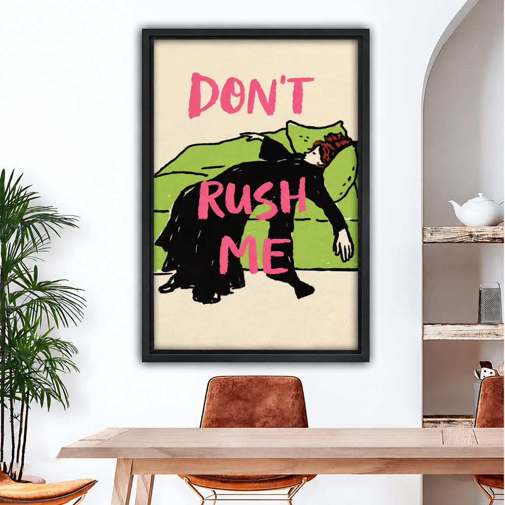 Framed canvas of retro illustration of a woman in black dress sprawled over a green sofa with bold pink "Don't Rush Me" lettering on cream background above wood dining table with leather chairs