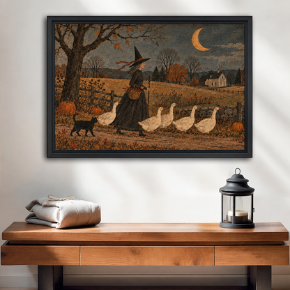 Black-framed folk art witch and geese wall art above a wooden console beside folded linens and a candle lantern.