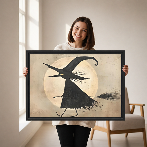Framed flying witch moon canvas wall art displayed above a wooden console with a lantern and folded blanket