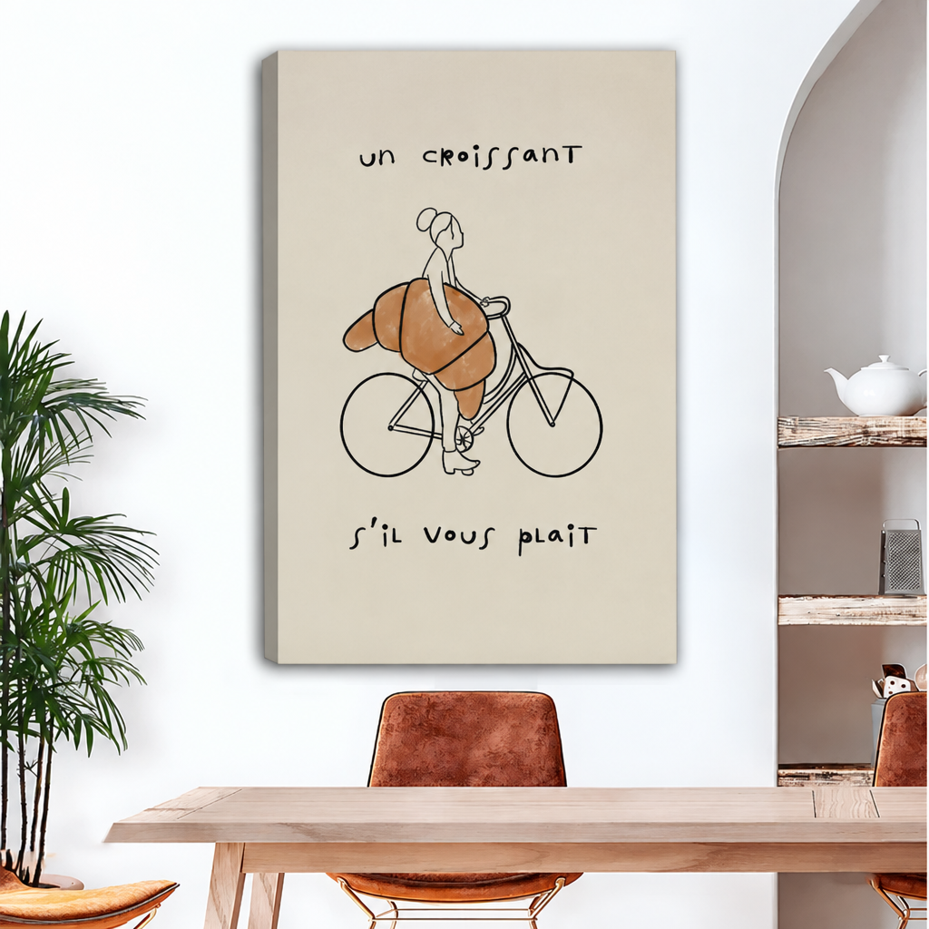 Frameless gallery wrap canvas of whimsical line drawing of a woman on a bicycle with an oversized golden croissant and French quote on warm cream background above wood dining table with brown leather chairs