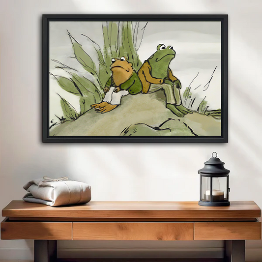 Black-framed frog friends canvas wall art showing two seated companions beneath a tree above a wooden console.