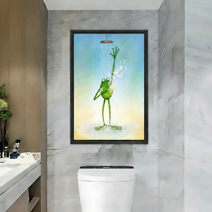 Framed canvas wall art of whimsical green frog showering with raised arm and soap bubbles, hung above toilet in marble bathroom