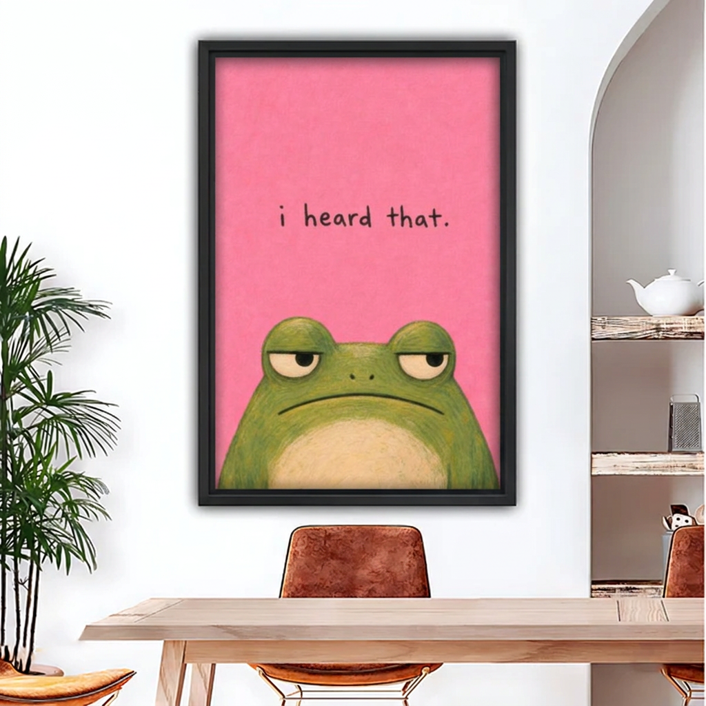 Black-framed funny pink frog canvas wall art with “i heard that” lettering above a wooden dining table