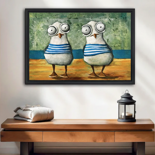 Funny whimsical seagull duo in blue striped sailor shirts, black framed canvas wall art hung above a wooden entryway console table