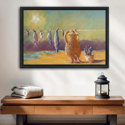 Black framed oil painting canvas of a fluffy ginger cat reaching up to a clothesline hung with dried fish on a golden sandy beach, with a small pot of fish beside it, displayed above a wooden console table with a lantern