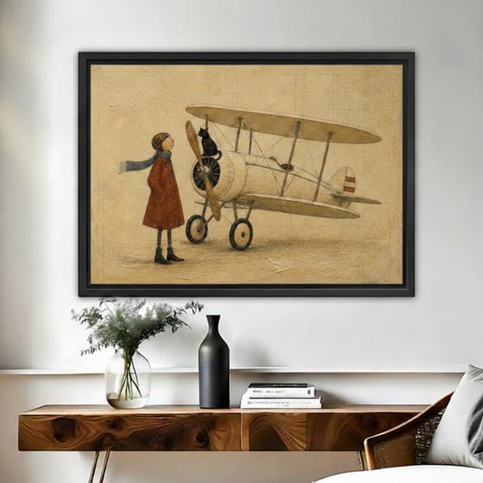 Black framed vintage-style canvas of a whimsical girl in a red coat and aviator goggles standing beside a cream biplane with a black cat perched on the propeller, displayed above a walnut console table with a black vase and white floral arrangement