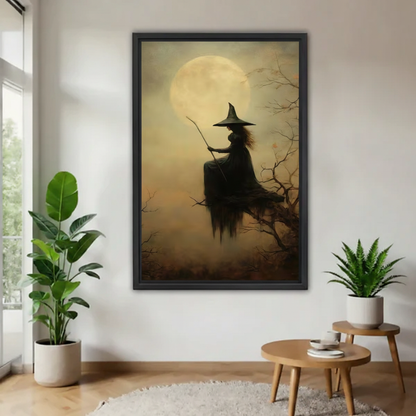 Witch silhouette in pointed hat seated on bare tree branches with broomstick before glowing full moon in amber mist framed canvas above round wood coffee table with white sofa