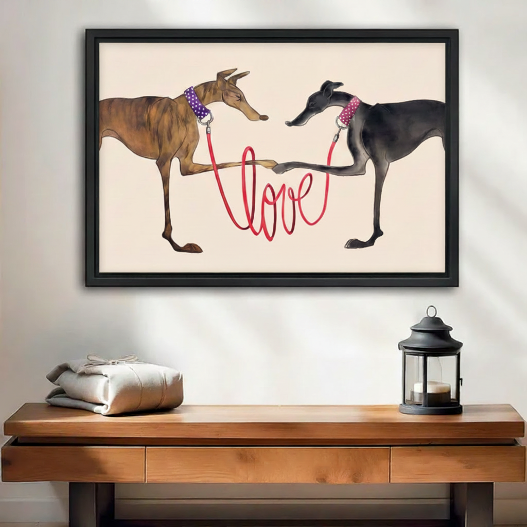 Two greyhounds with red love leash framed wall art print, black frame, whimsical dog love illustration cream background, hung above a wooden console table with lantern in a bright minimalist entryway