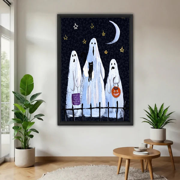 Halloween three white sheet ghosts trick or treat black cat pumpkin lantern crescent moon star sky black framed canvas wall art on white wall beside round wood side table with two green tropical plants