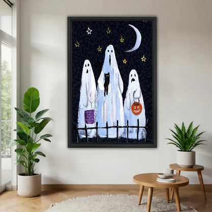 Halloween three white sheet ghosts trick or treat black cat pumpkin lantern crescent moon star sky black framed canvas wall art on white wall beside round wood side table with two green tropical plants
