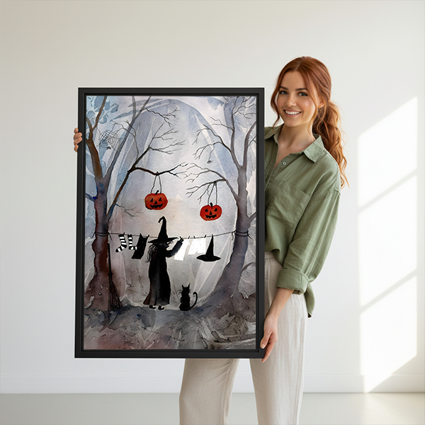 Halloween witch and cat canvas wall art with dangling jack-o'-lanterns in a black frame beside houseplants.